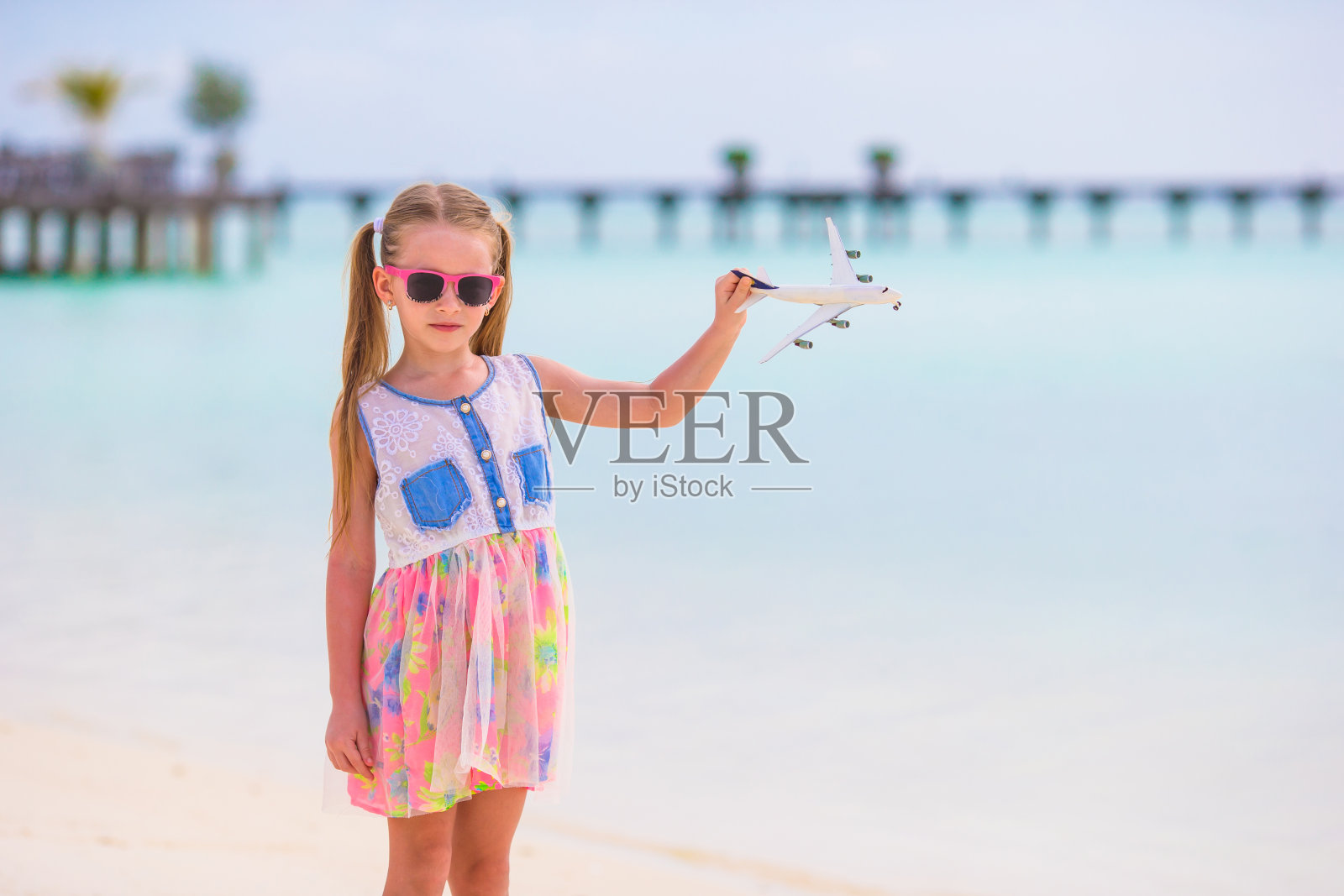 白色的沙滩上，小女孩手里拿着玩具飞机照片摄影图片