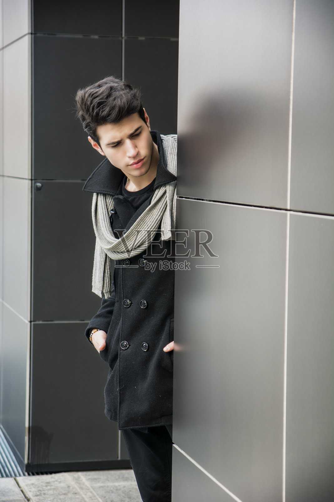 穿着冬季时装的时髦英俊的年轻人靠墙站着照片摄影图片