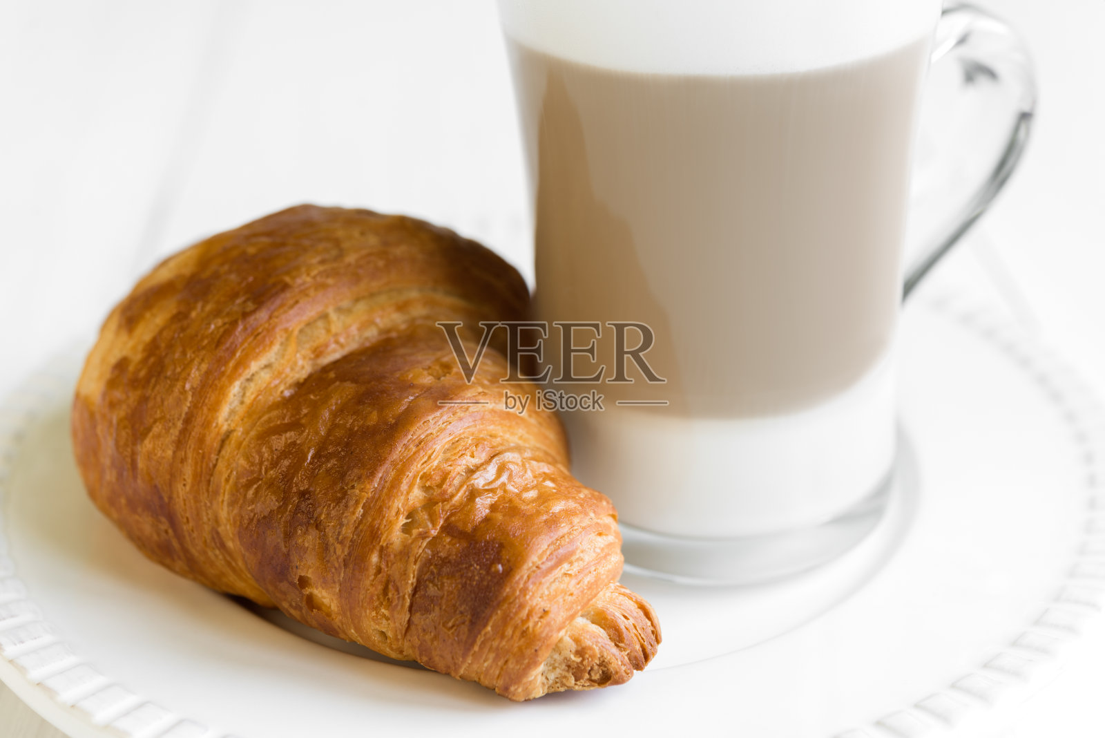 白盘子里放着牛角面包和一杯拿铁咖啡照片摄影图片