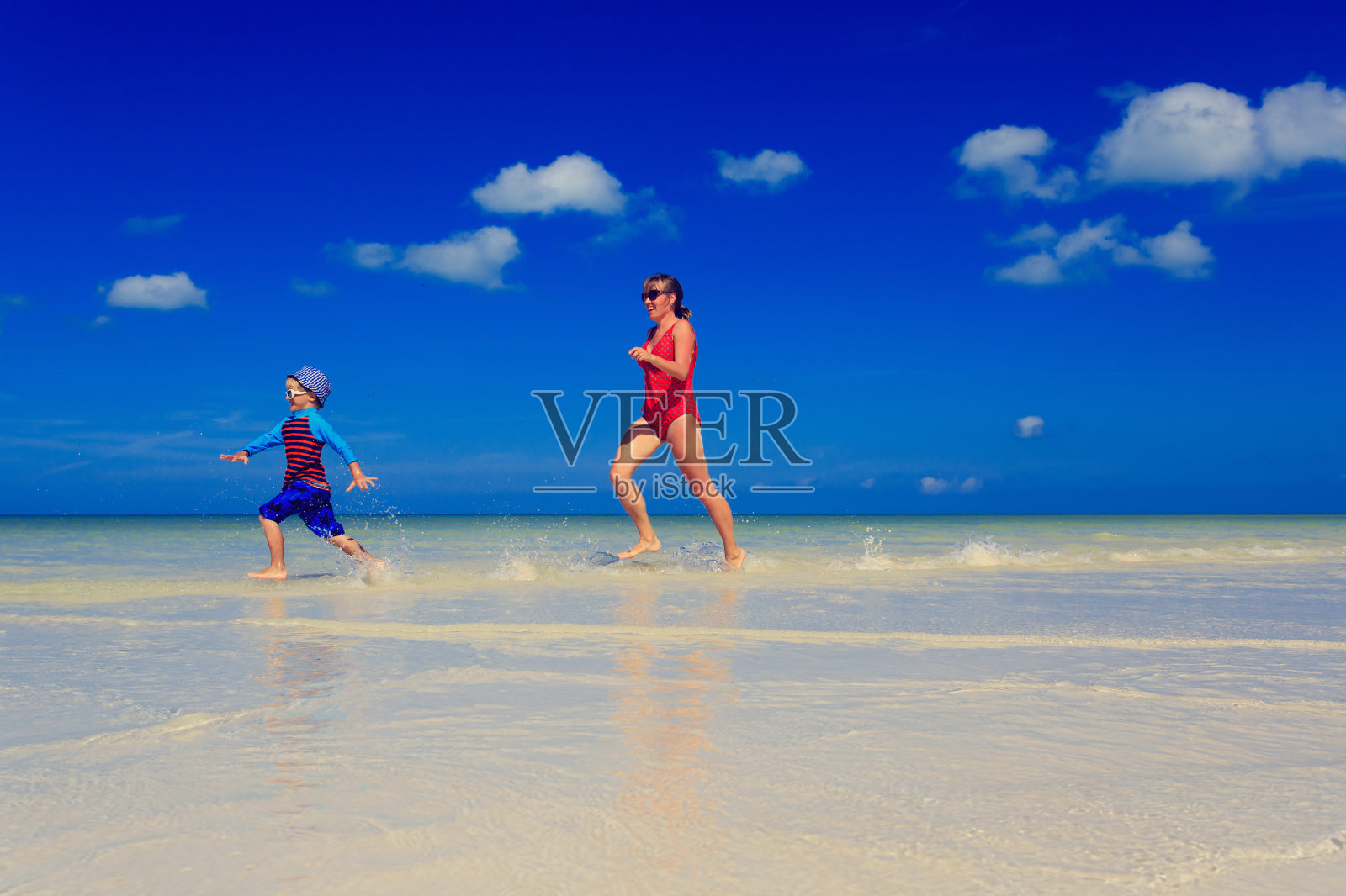 母亲和儿子在夏天的海滩上的水里奔跑照片摄影图片