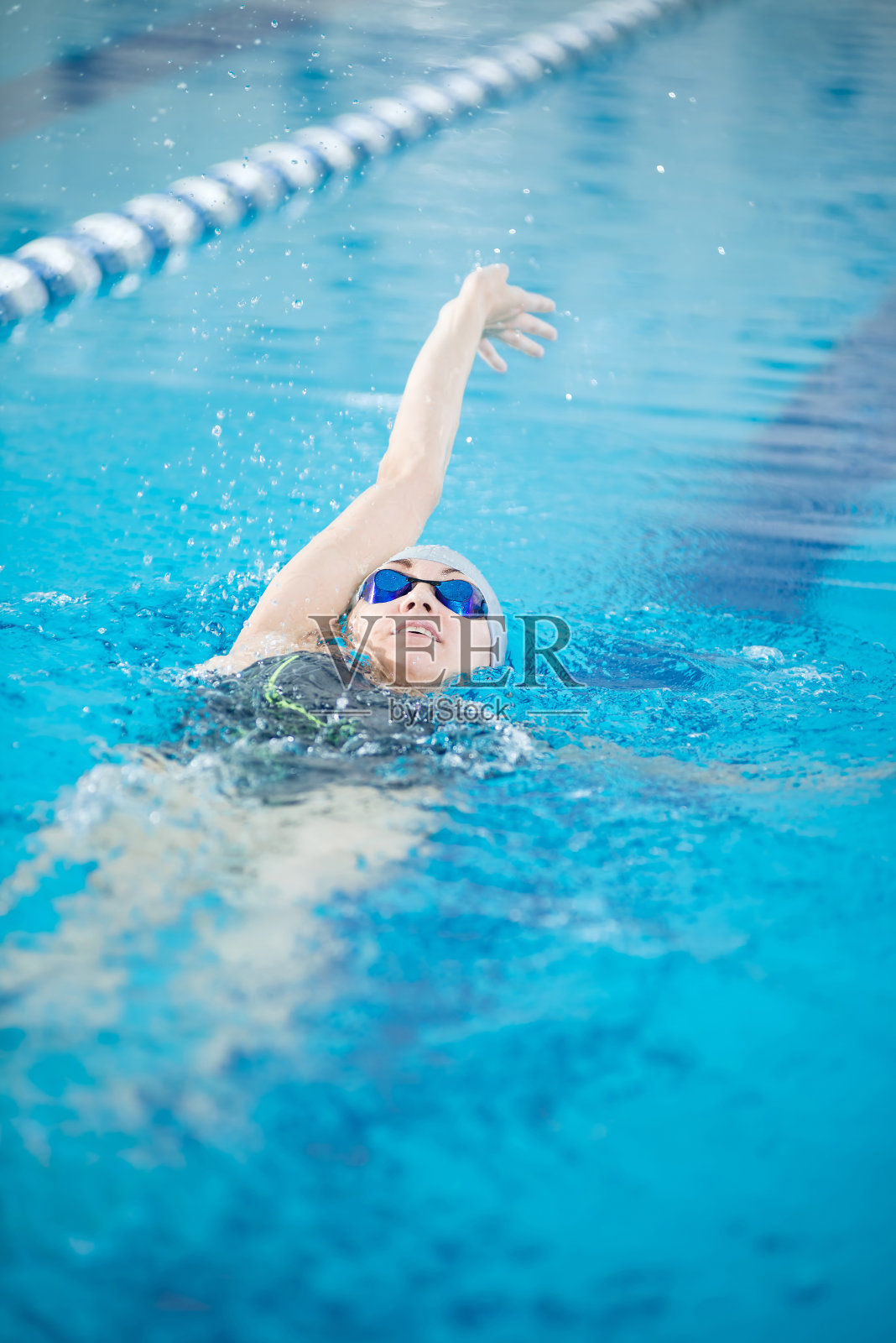 年轻的女孩戴着护目镜，以爬泳的姿势仰泳照片摄影图片