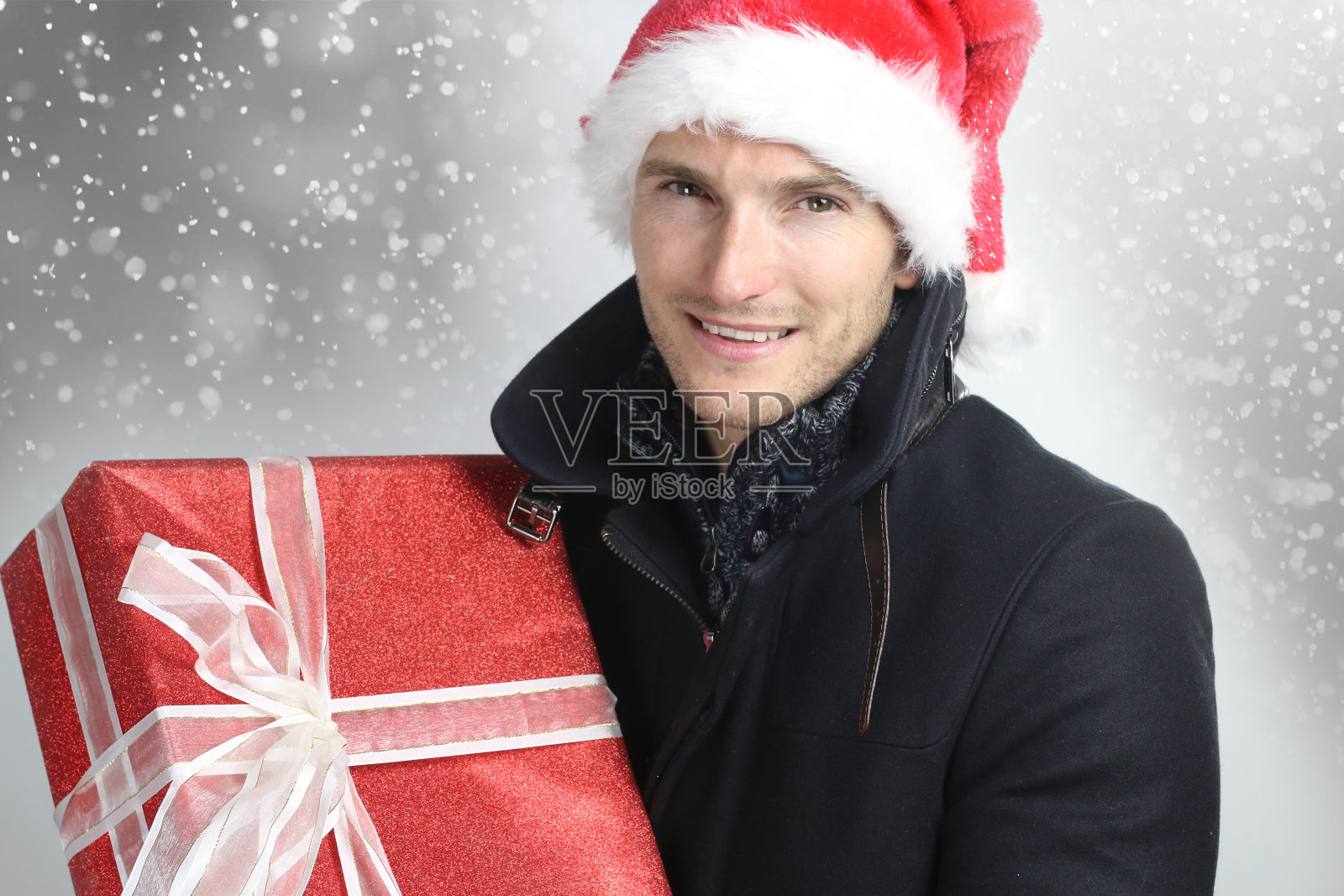 一个英俊的男人在灰色的背景下拿着圣诞礼物照片摄影图片