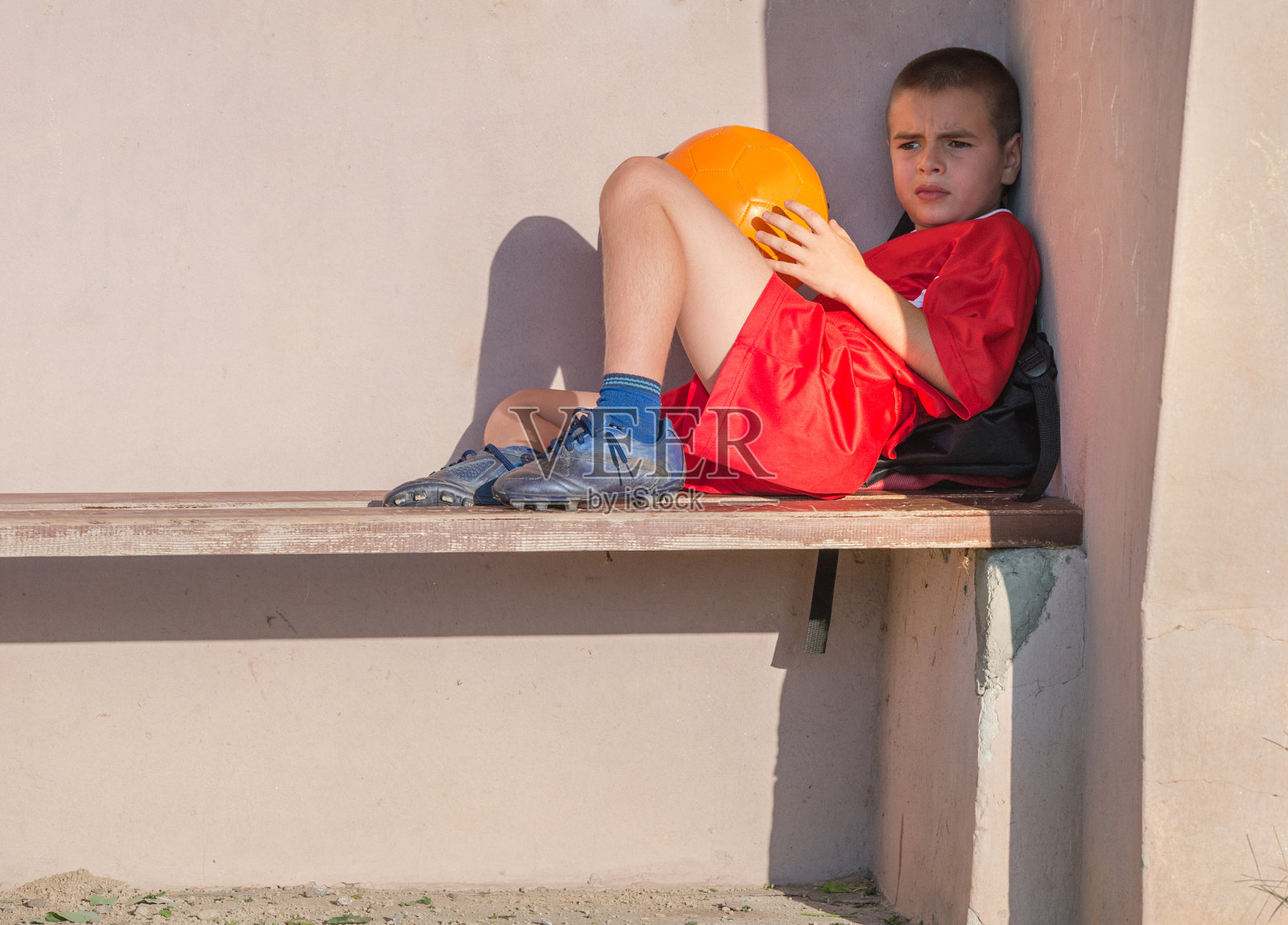 穿着红色足球衫的男孩坐在长凳上照片摄影图片
