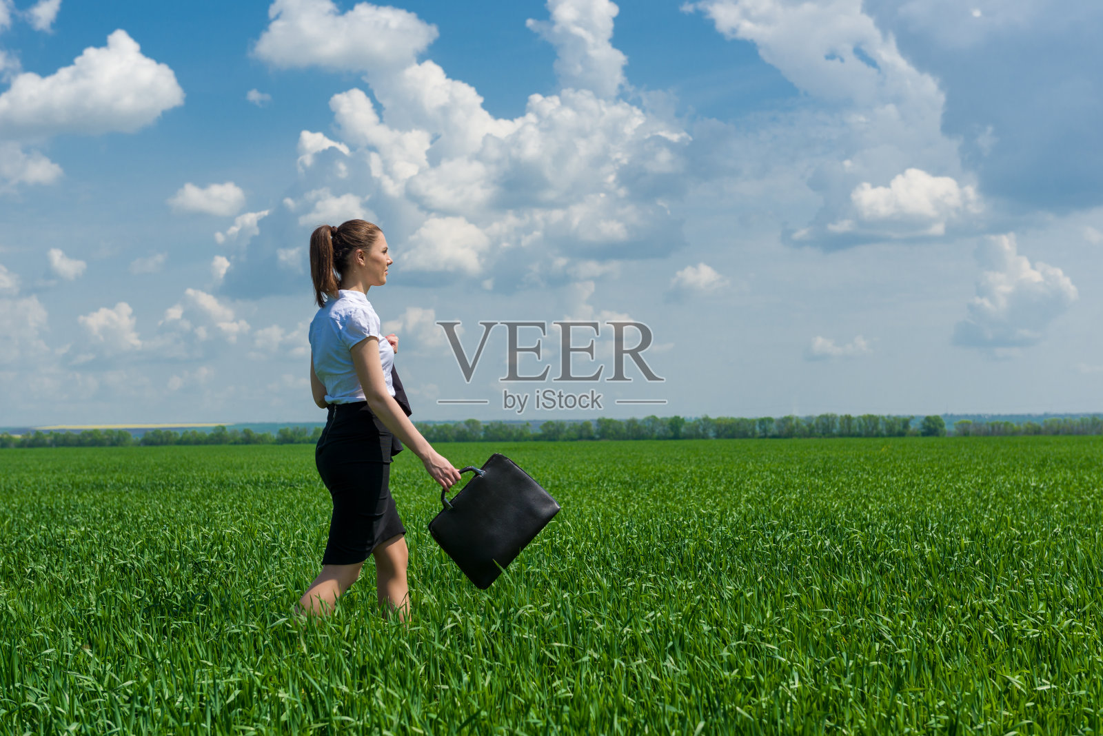 拿着公文包的女孩在草地上走照片摄影图片