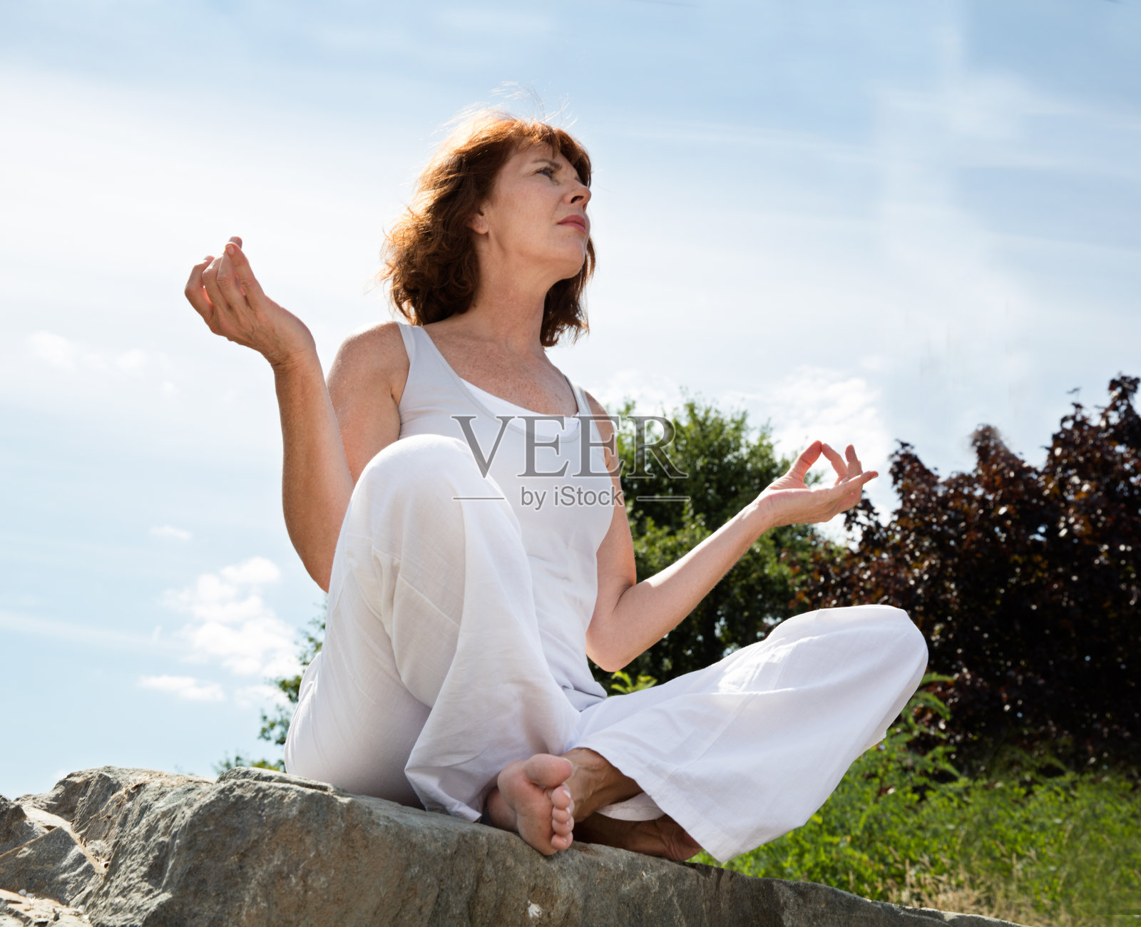 在户外的一块石头上用瑜伽姿势呼吸着成熟的女人照片摄影图片