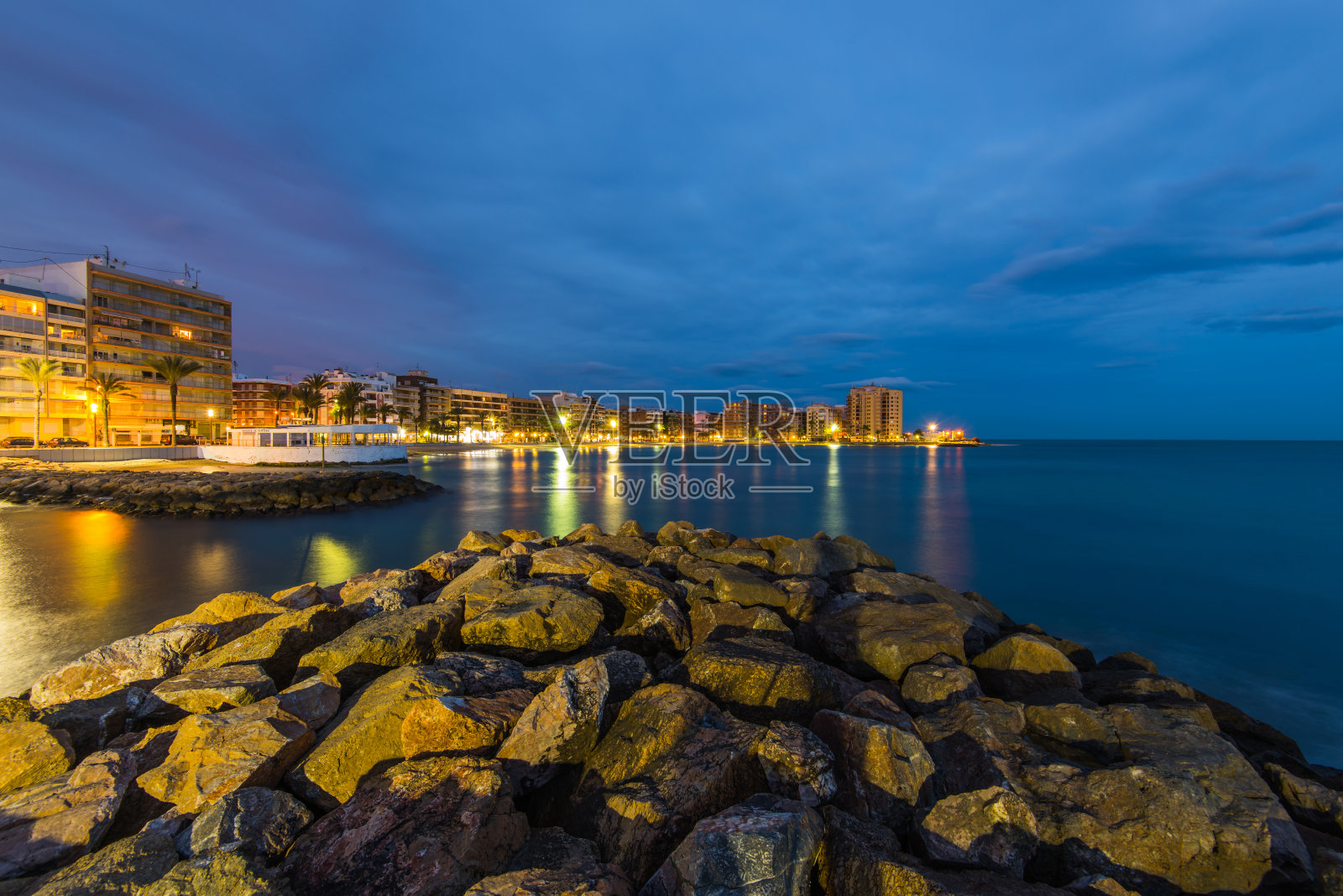 西班牙托雷维哈的岩石海滩和灯火通明的城市照片摄影图片