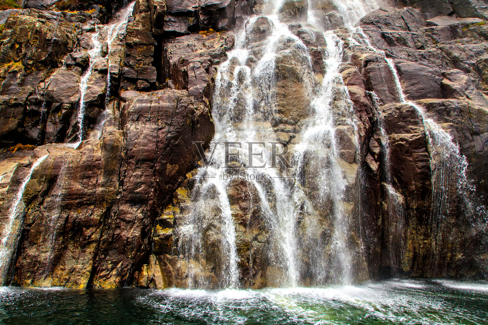 瀑布汇流入海中，溅起水花和泡沫照片摄影图片
