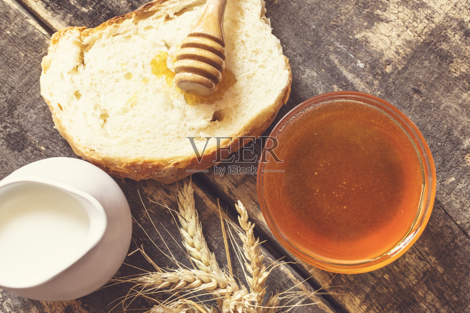 蜂蜜在罐子里，面包，小麦和牛奶在桌子上。照片摄影图片