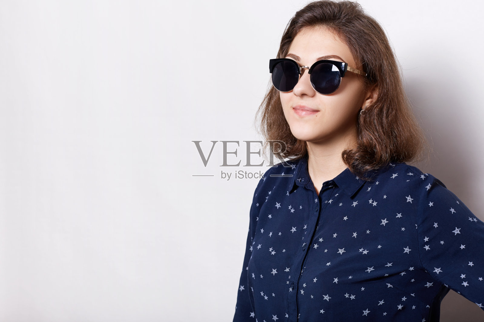 一个优雅的黑发美人的肖像戴着墨镜和时尚的衬衫有快乐的表情，而摆姿势的白色背景与复制空间为你的文本或广告内容。照片摄影图片