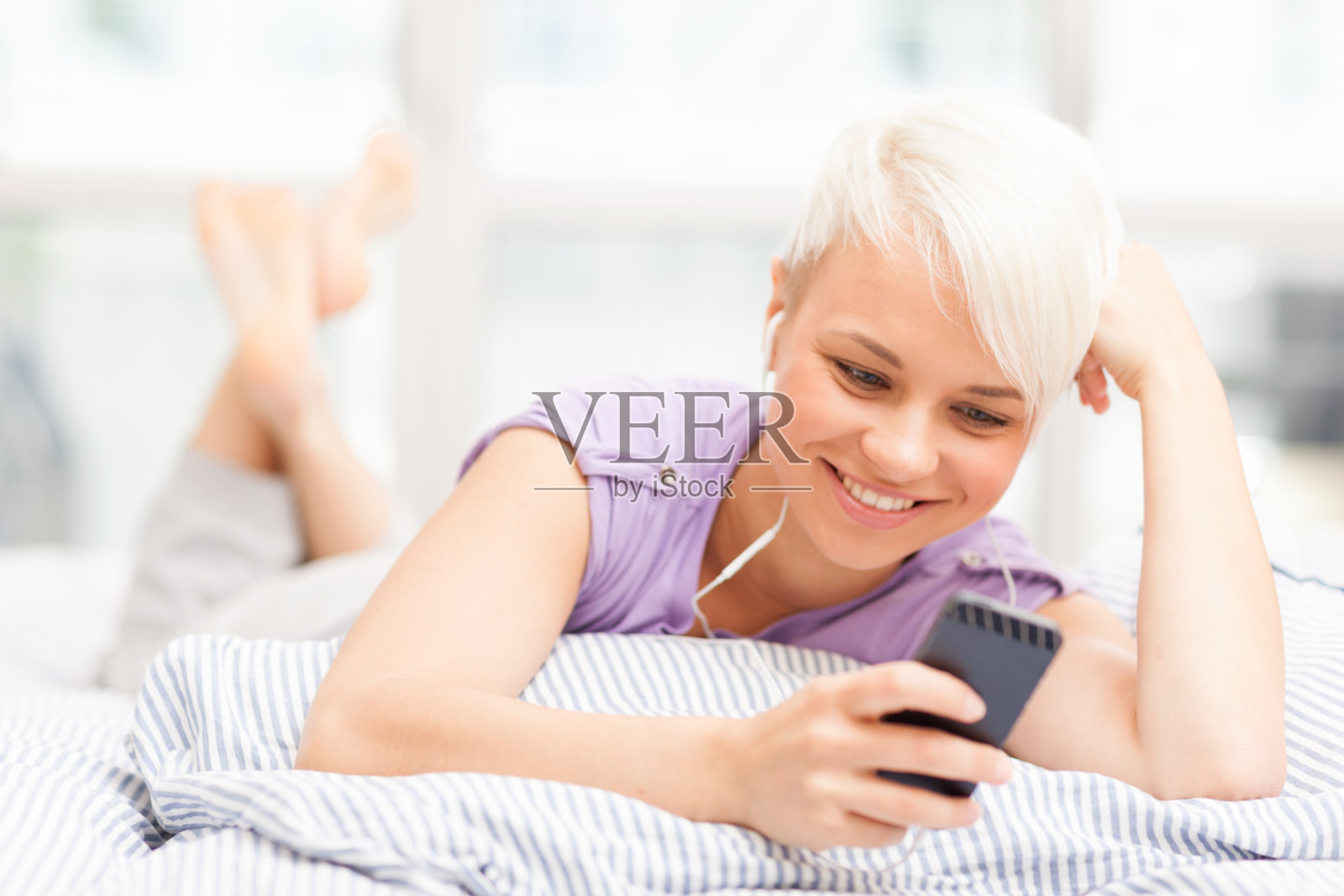 年轻女子戴着耳机在床上打电话照片摄影图片