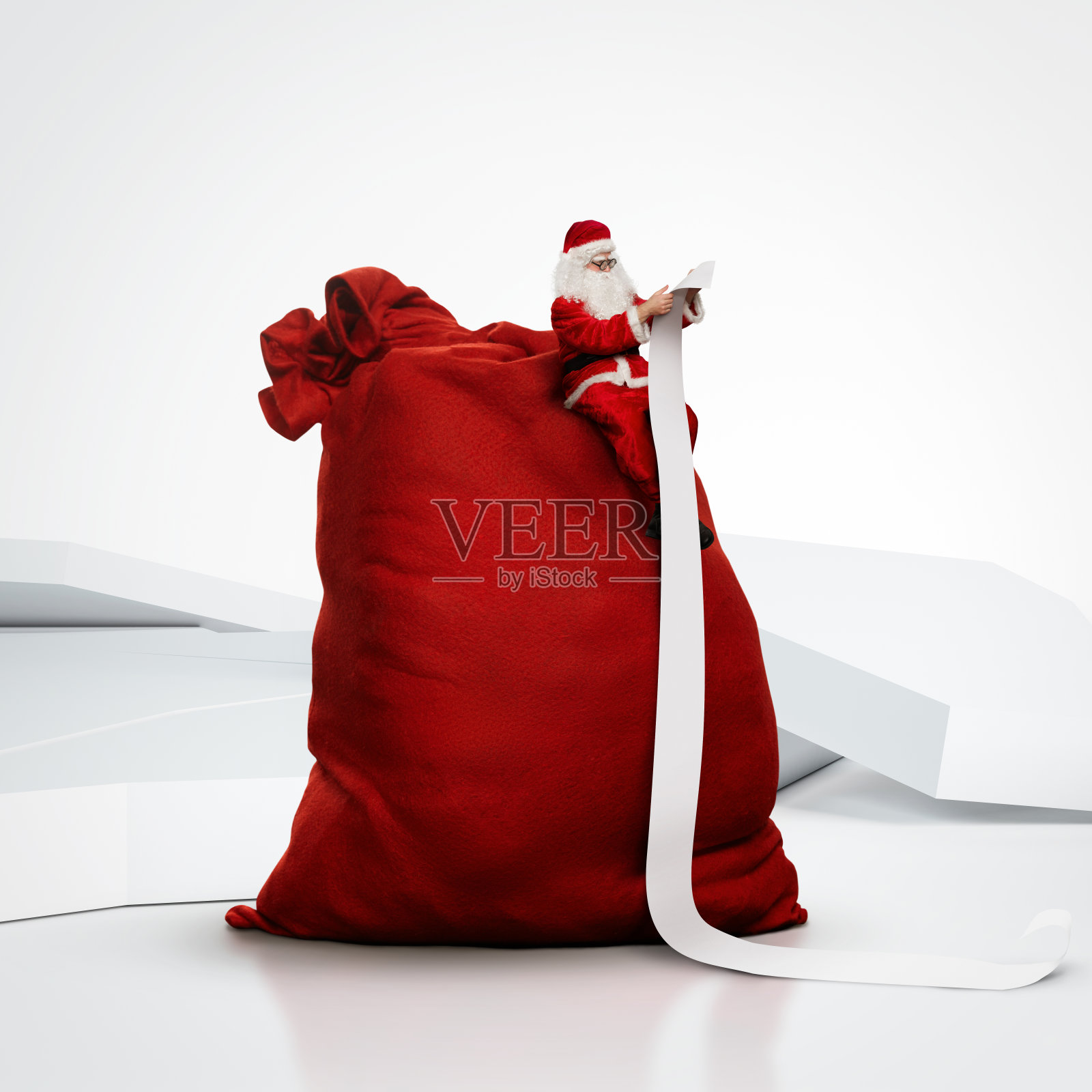 圣诞老人坐在大麻袋上读长长的清单照片摄影图片