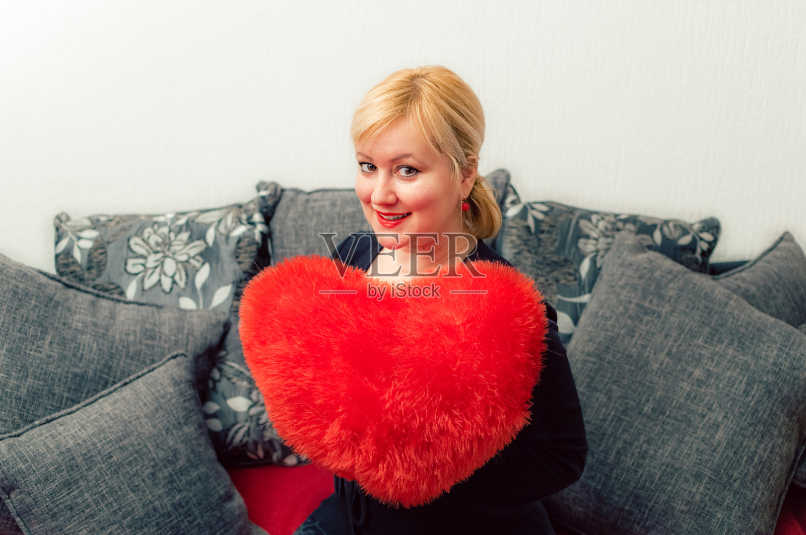 金发女人，红色心形枕头。圣瓦伦丁国际妇女节，三月八日庆祝。照片摄影图片