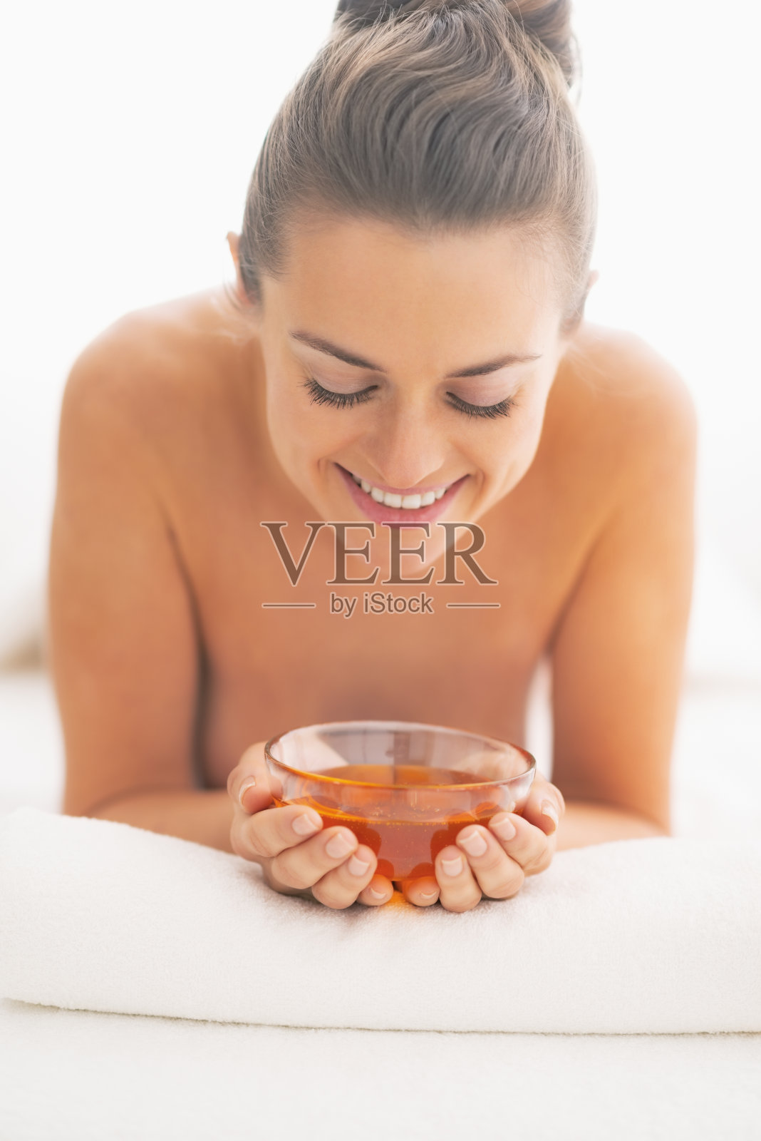 年轻女子在按摩台上，手里拿着一个盛有蜂蜜的盘子照片摄影图片