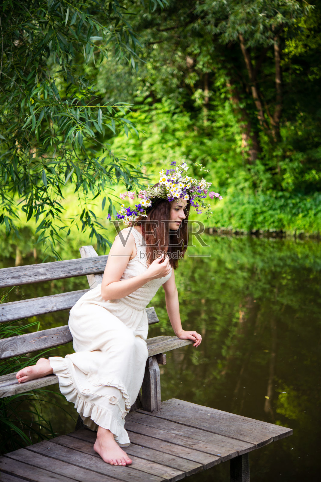 戴着花圈的女孩坐在长凳上望着河照片摄影图片