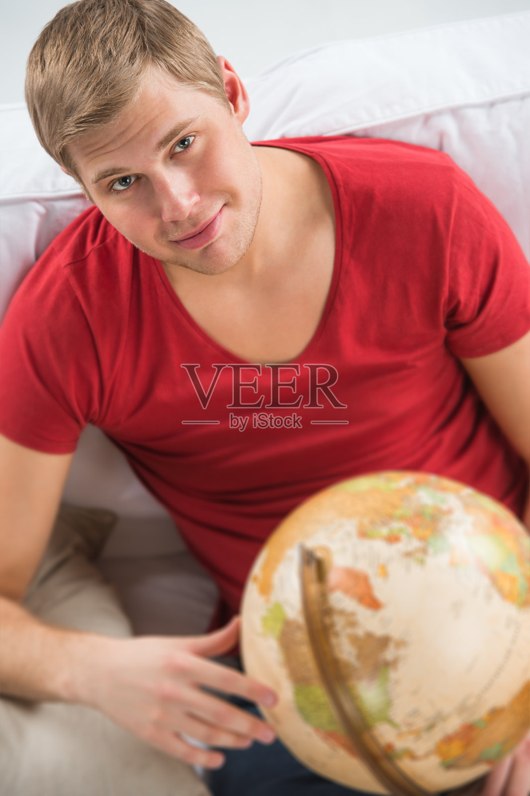 英俊的年轻人在沙发上的肖像与地球仪照片摄影图片