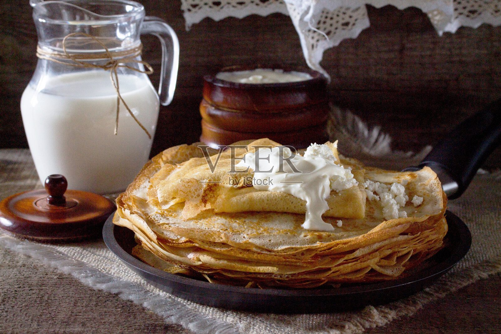 木桌上堆着煎饼、酸奶油和牛奶。照片摄影图片