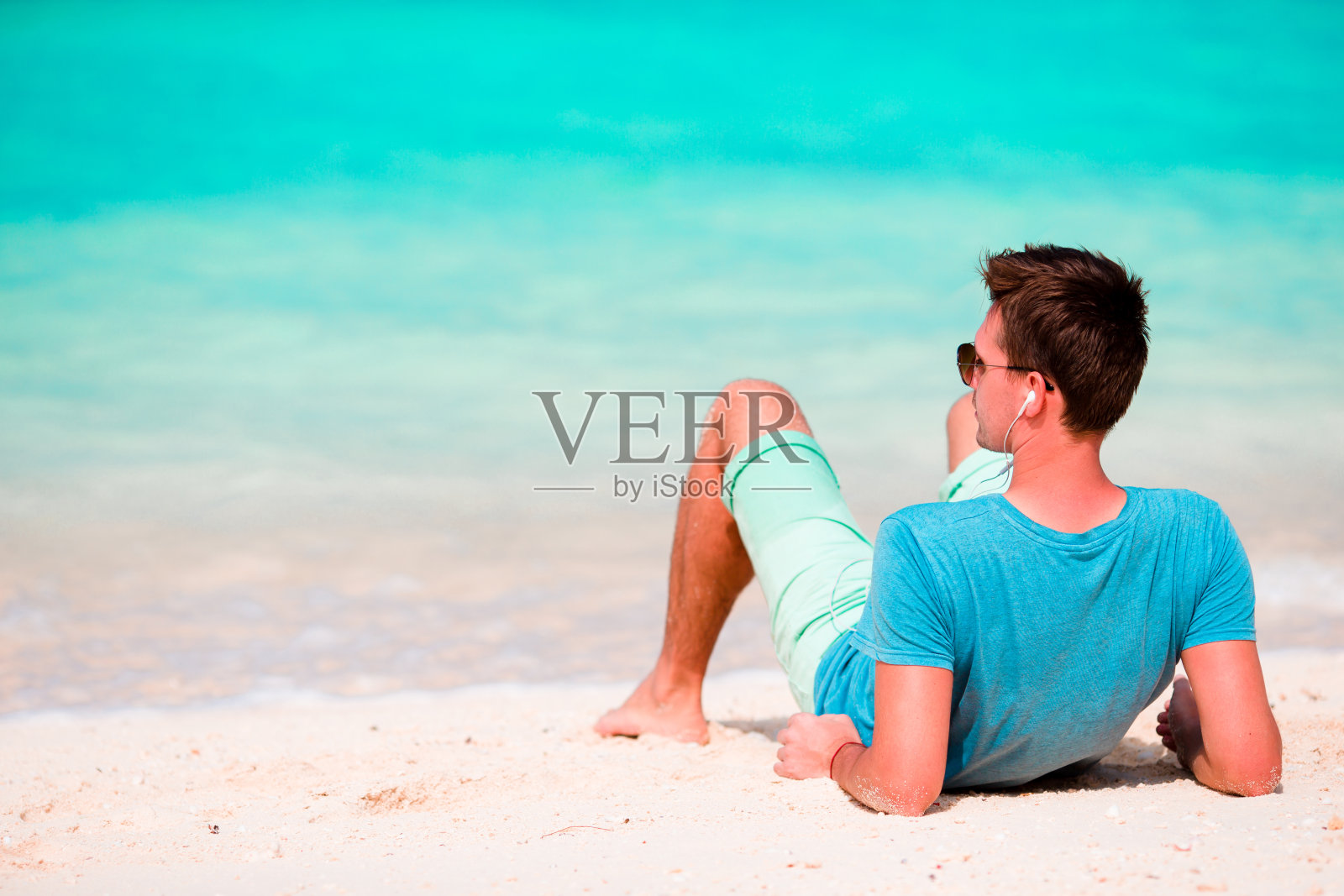 一个快乐的年轻人在白色的沙滩上欣赏音乐照片摄影图片