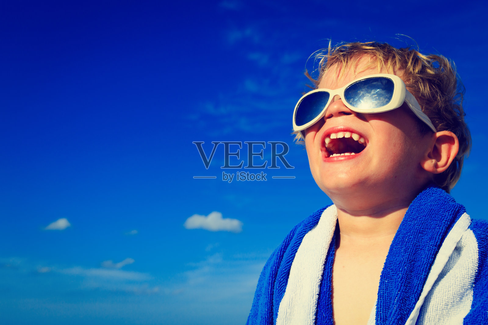 小男孩笑着裹在沙滩浴巾上的天空照片摄影图片