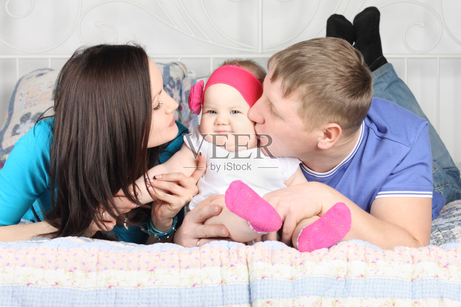 爸爸，美丽的妈妈亲吻可爱的宝宝，躺在床上照片摄影图片