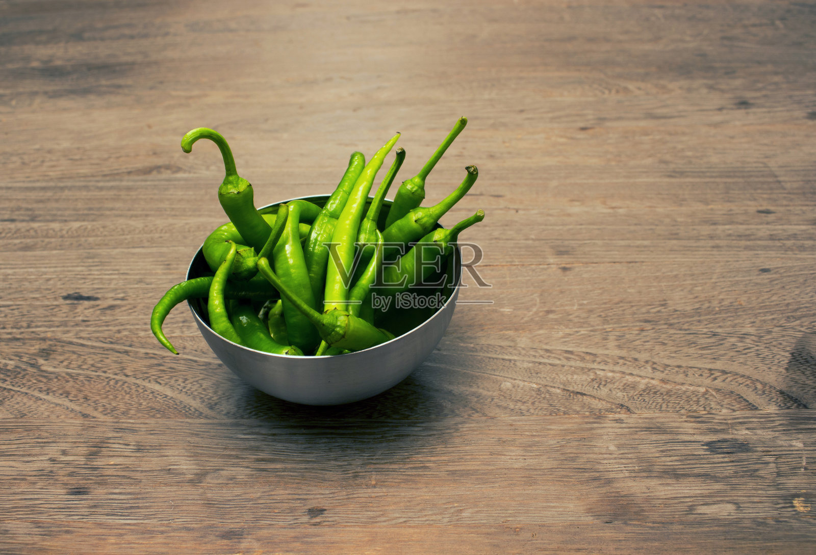 金属碗里的青椒放在木桌上照片摄影图片