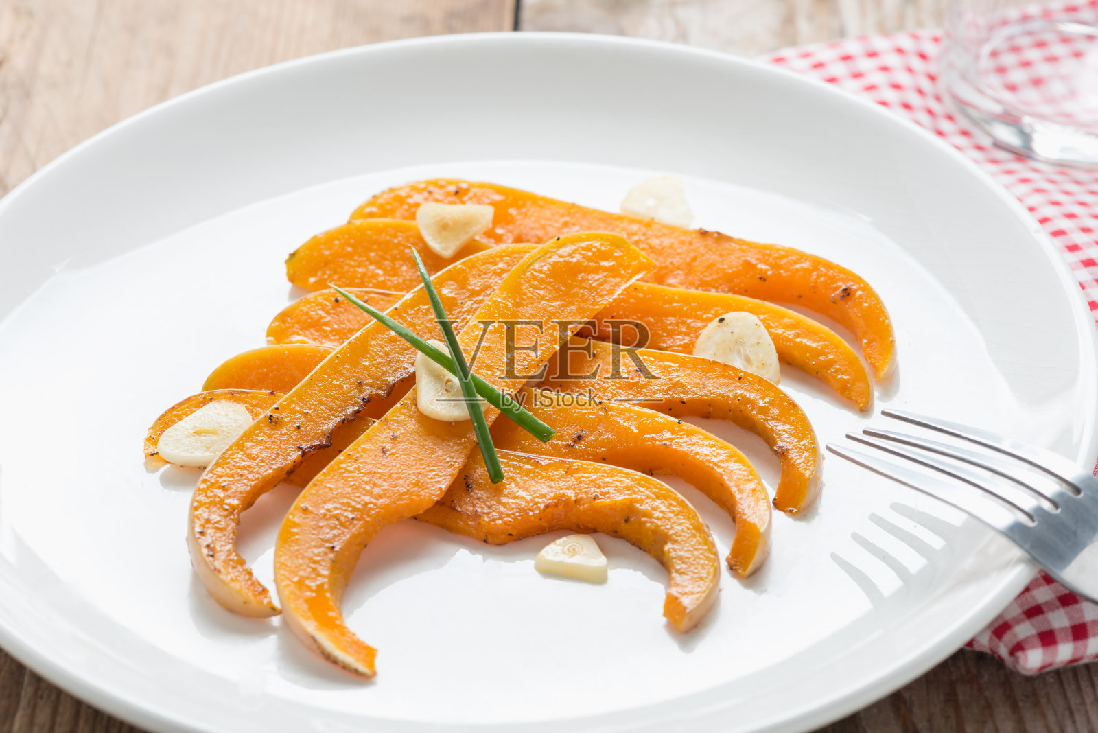 烤冬南瓜片和大蒜在白色盘子。照片摄影图片