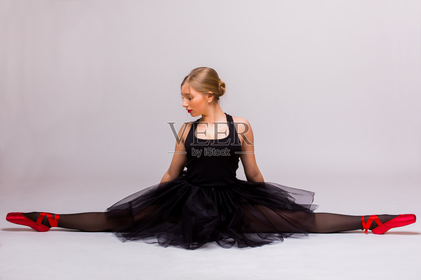 金发美丽的女孩在黑色芭蕾舞裙做体操分裂。照片摄影图片