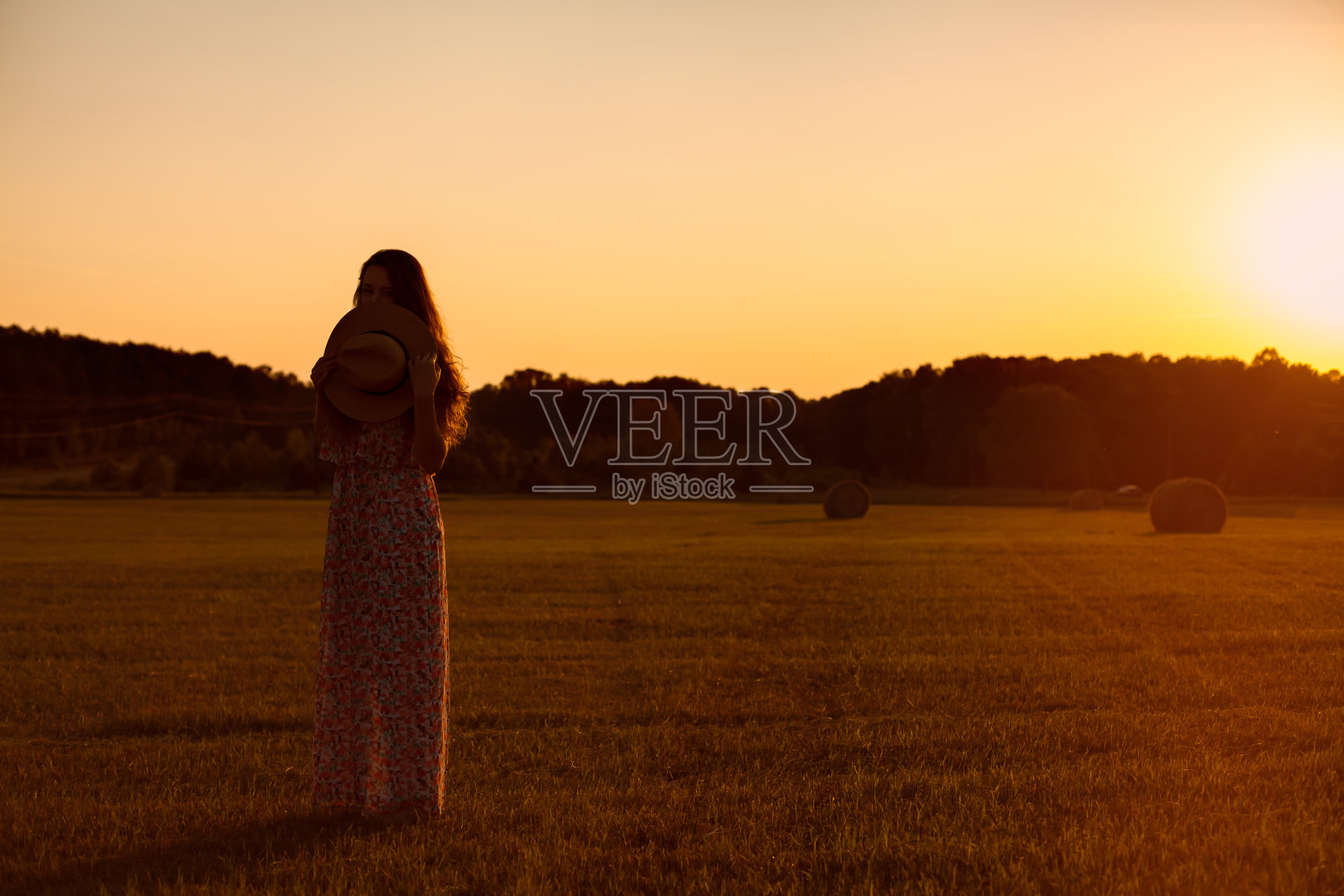 漂亮的年轻女子手里拿着帽子站在田野里。照片摄影图片