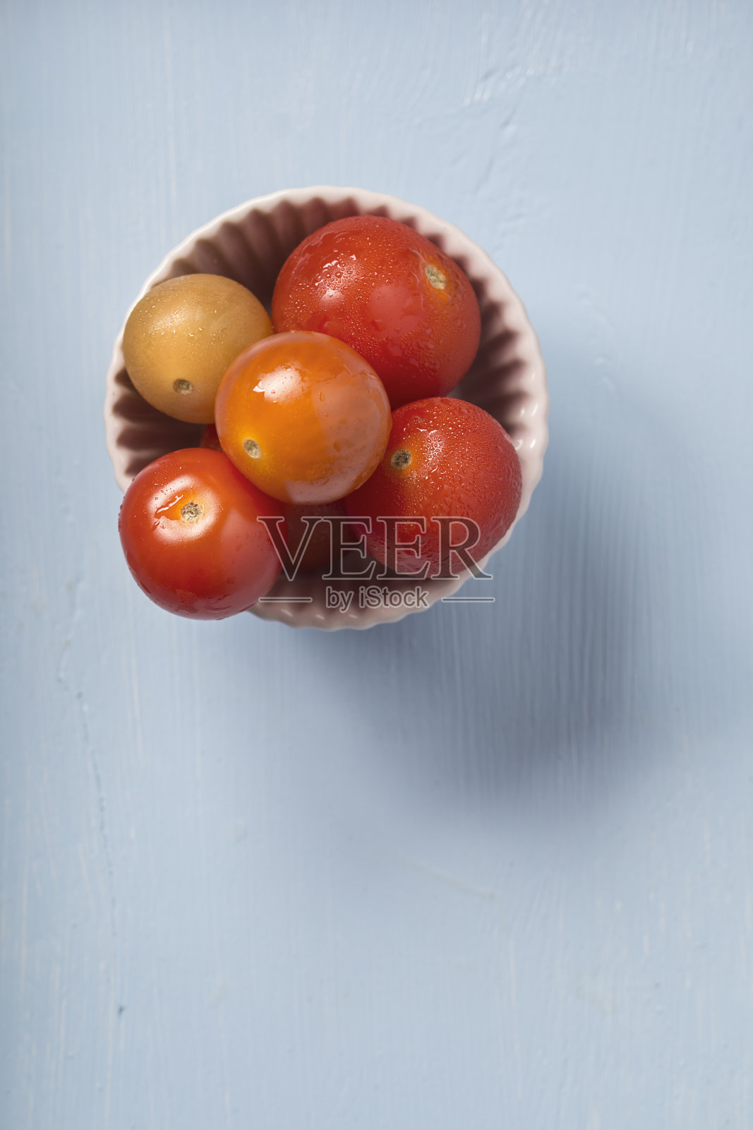 在蓝色木质背景上的一个碗里放番茄和樱桃照片摄影图片