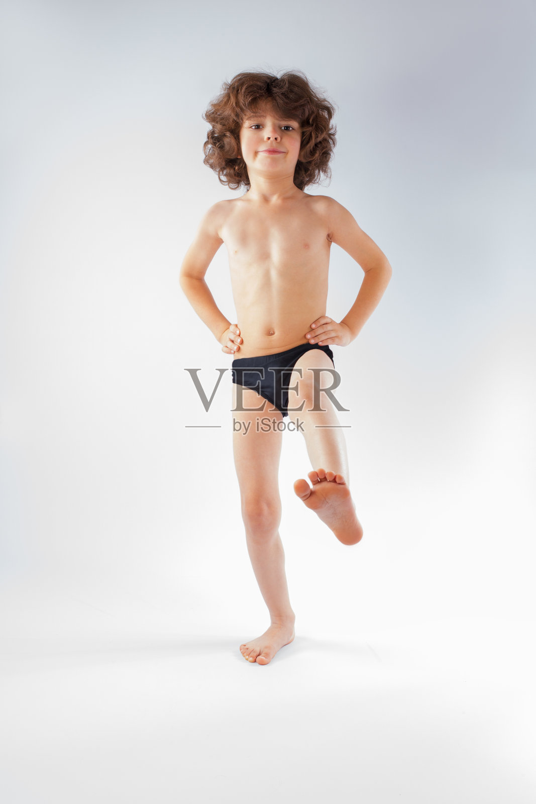 穿着游泳衣的卷发小男孩正在抬起他的腿。照片摄影图片