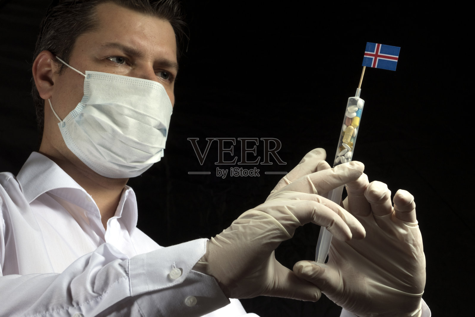 年轻男子作为一名医生给黑色背景上的冰岛国旗进行医疗注射照片摄影图片