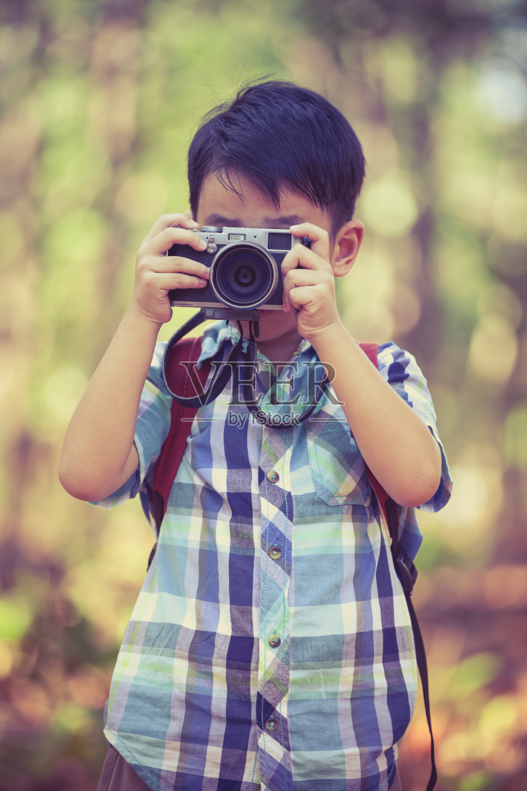 亚洲男孩与数码相机在美丽的户外。复古的风格。照片摄影图片