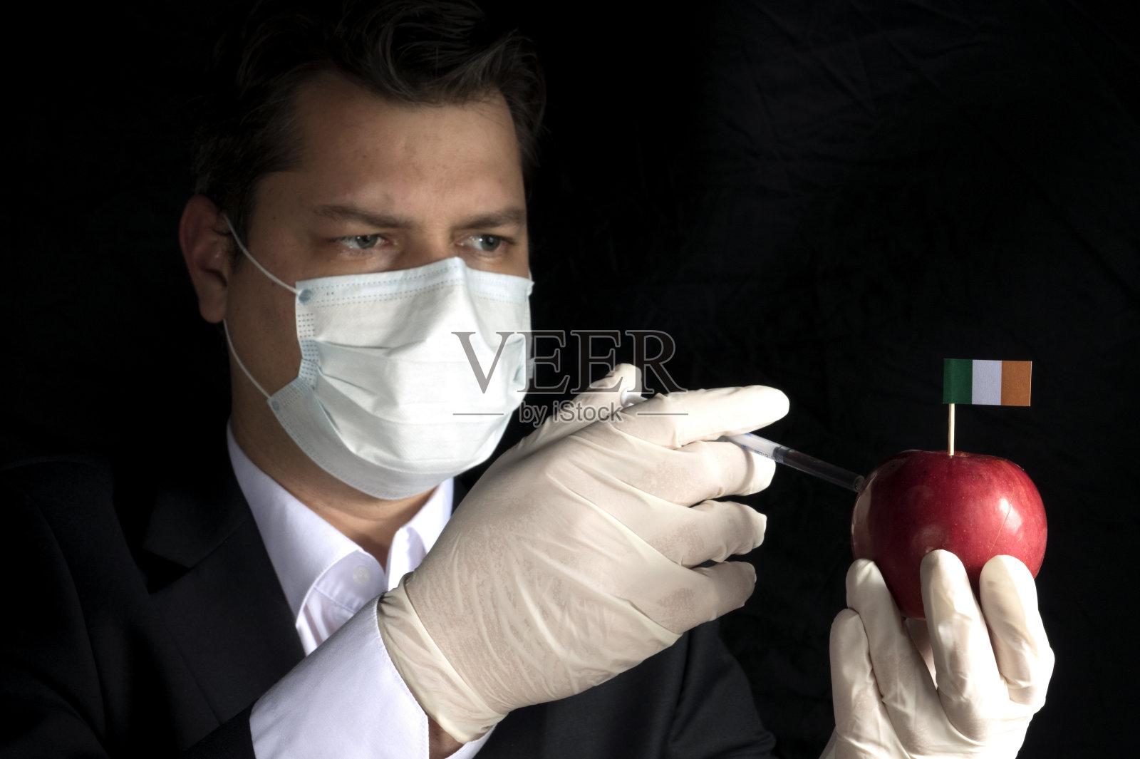 年轻的商人向黑色背景上有爱尔兰国旗的苹果注射化学物质照片摄影图片