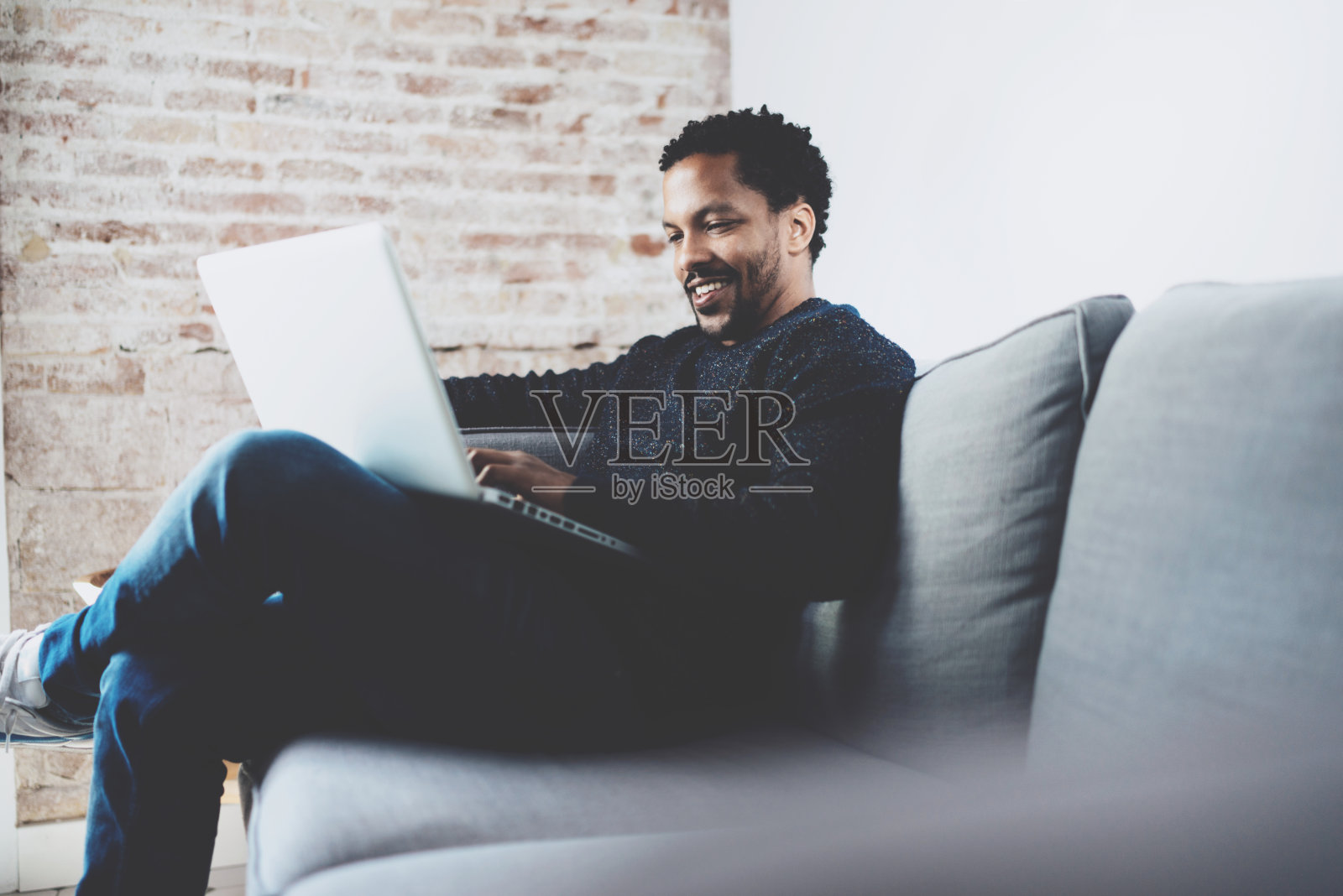 满脸胡须的非洲男子坐在沙发上用笔记本电脑工作照片摄影图片