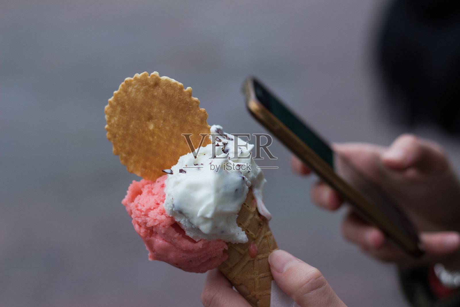 正在用手机的人，在模糊的背景下拿着冰淇淋照片摄影图片