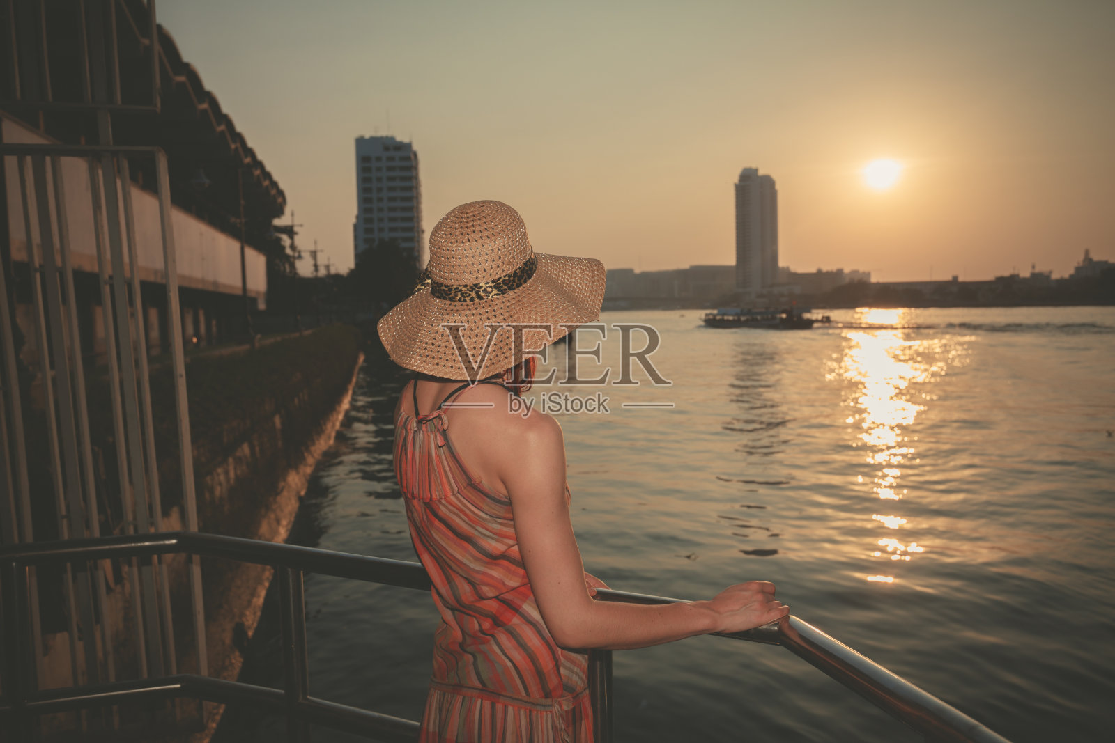 一个年轻女子在城市的河上欣赏日落照片摄影图片