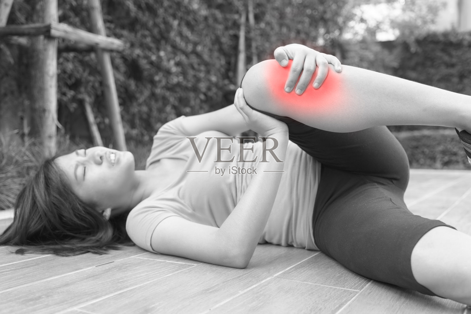 亚洲女子跑步者躺在地板上和触摸她受伤的膝盖-黑和白的概念。照片摄影图片