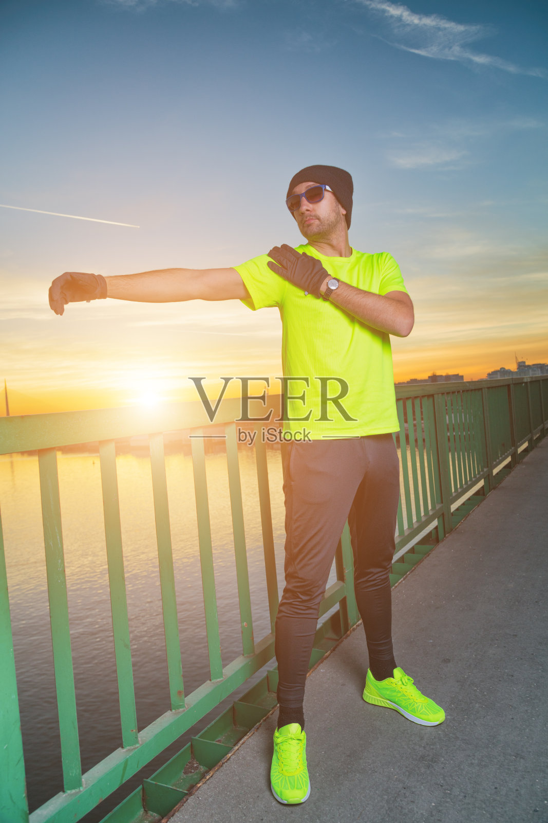 城市慢跑者在日落/日出时在桥上伸展。照片摄影图片