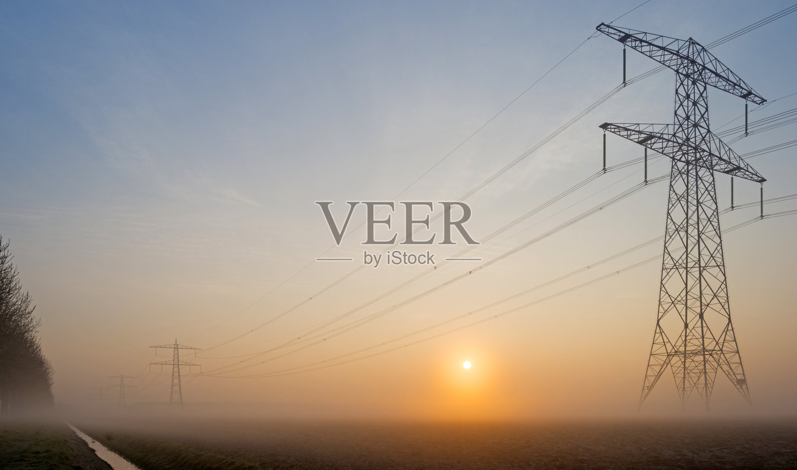 日出时分，在雾蒙蒙的田野里的输电线照片摄影图片