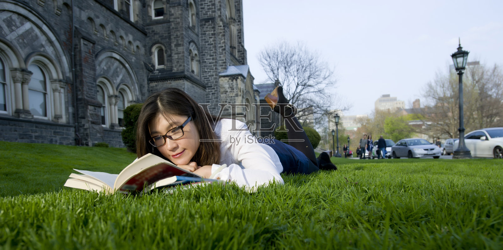 年轻的女学生在外面的草地上读课本照片摄影图片