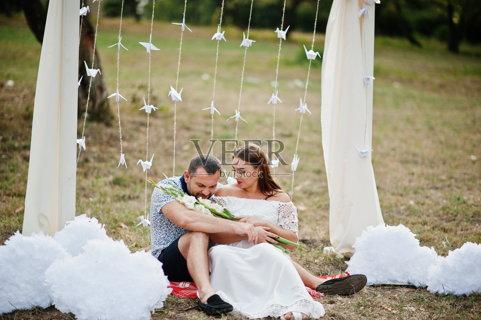 一对幸福的怀孕夫妇坐在花园的装饰拱门下照片摄影图片