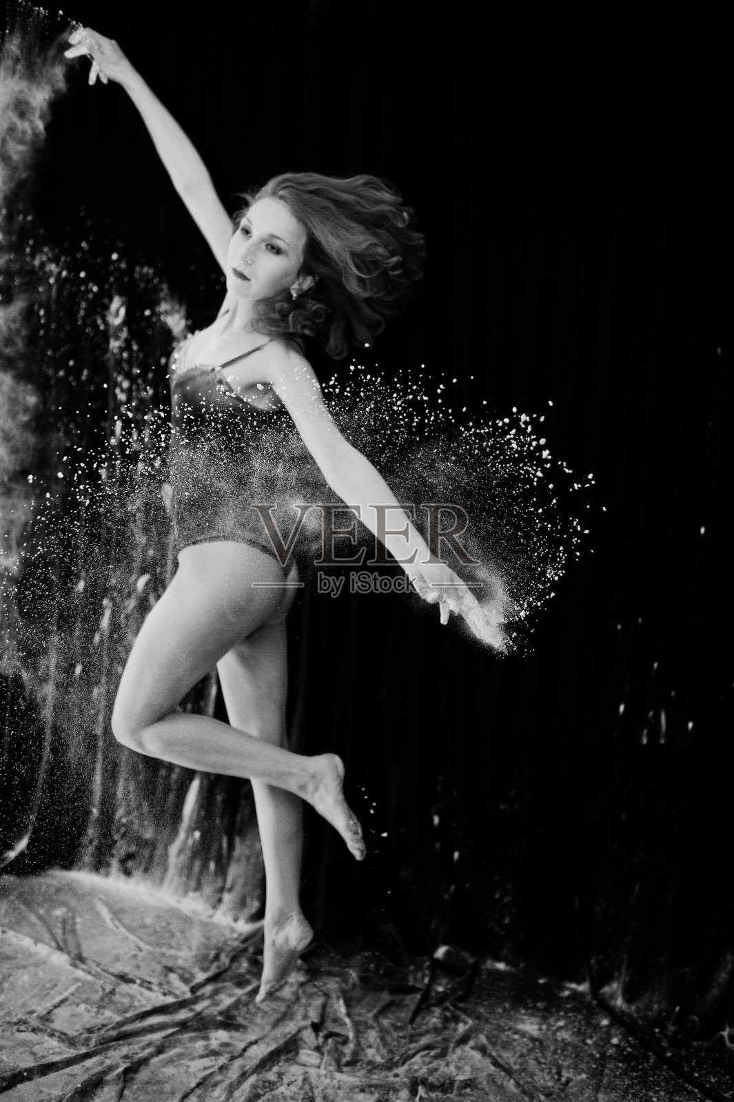 女孩舞者在白色的灰尘和面粉在黑色的背景跳舞。一名女子在面粉上跳舞。照片摄影图片