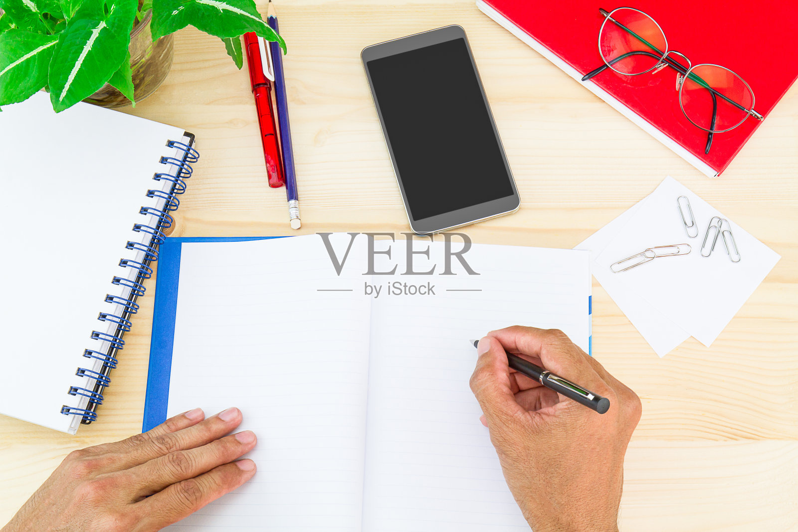 用办公用品在笔记本上写字，桌上放智能手机照片摄影图片