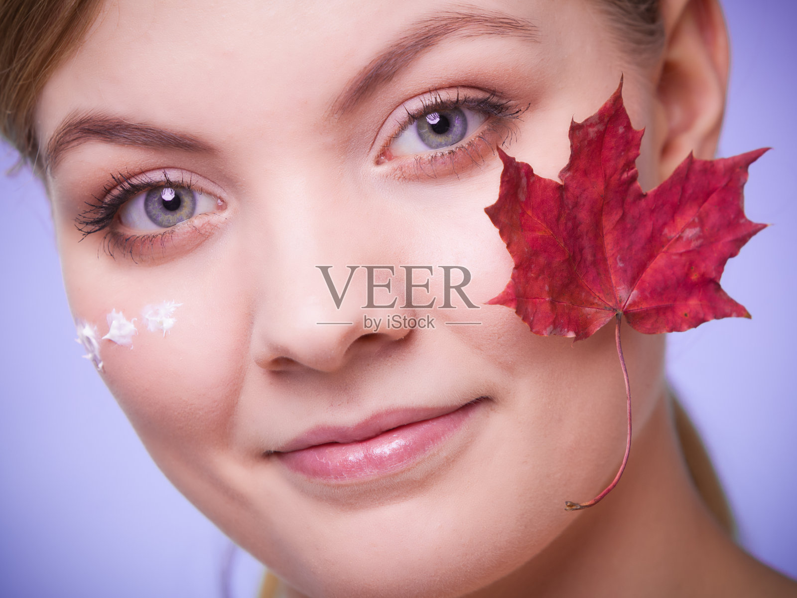 皮肤护理。年轻女子的脸上带着枫叶。照片摄影图片