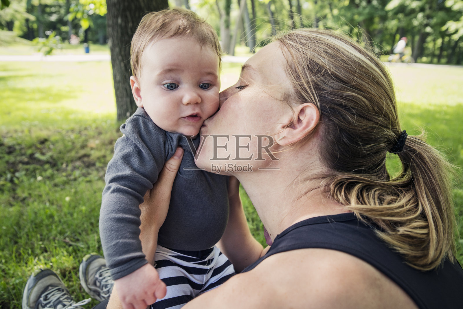 妈妈在夏天的公园亲吻小男孩。照片摄影图片
