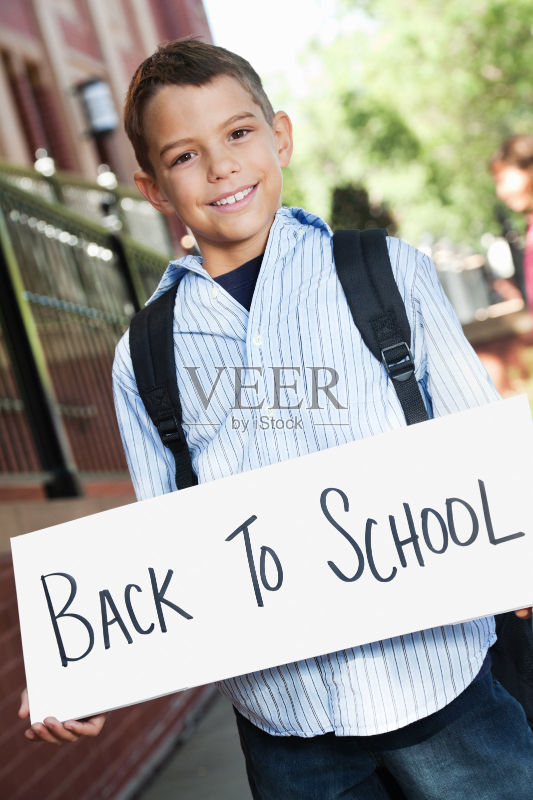 快乐的男孩在教育大楼外举着学校的牌子照片摄影图片