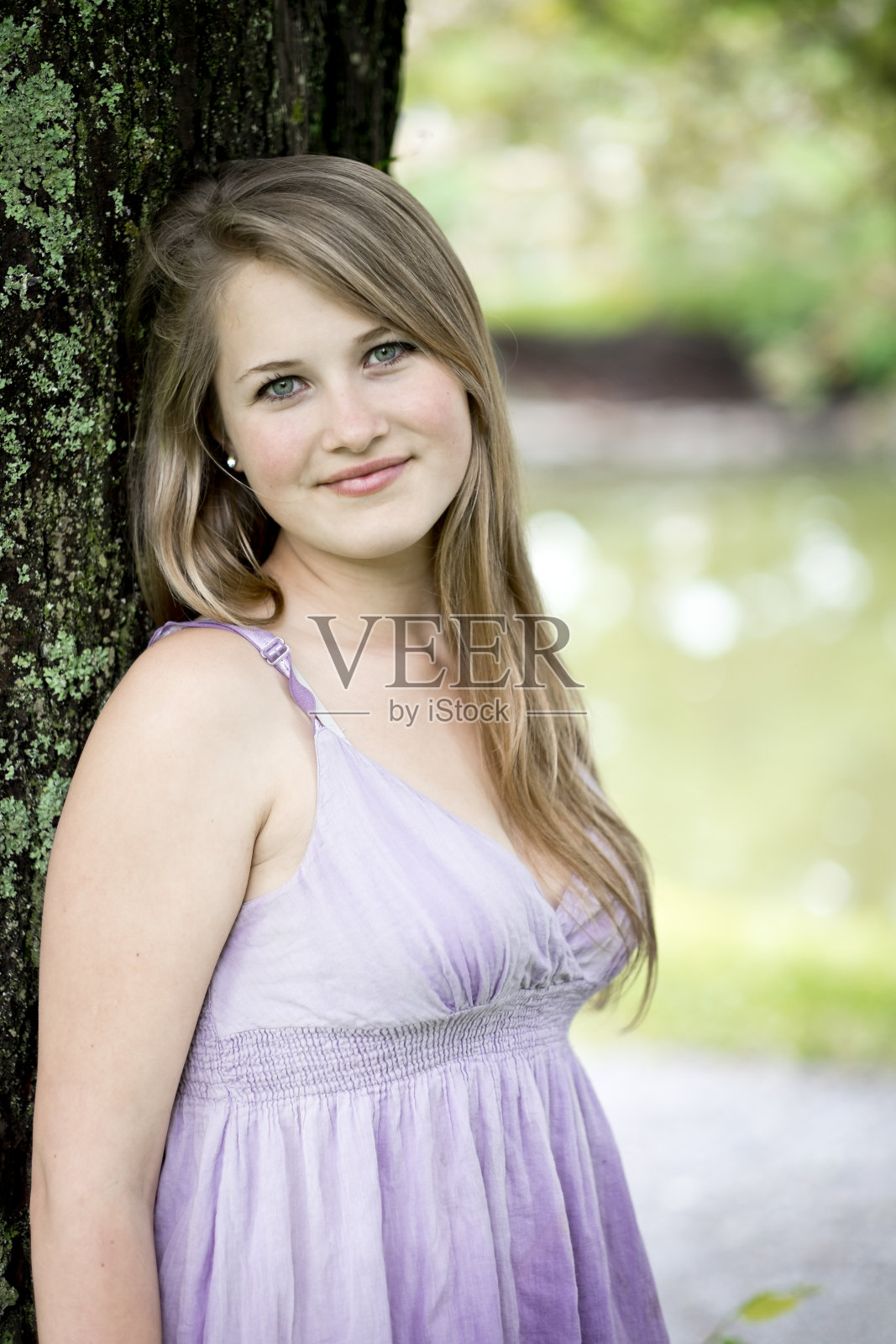 一个十几岁的女孩在一个正式的花园里倚在一棵树上。照片摄影图片