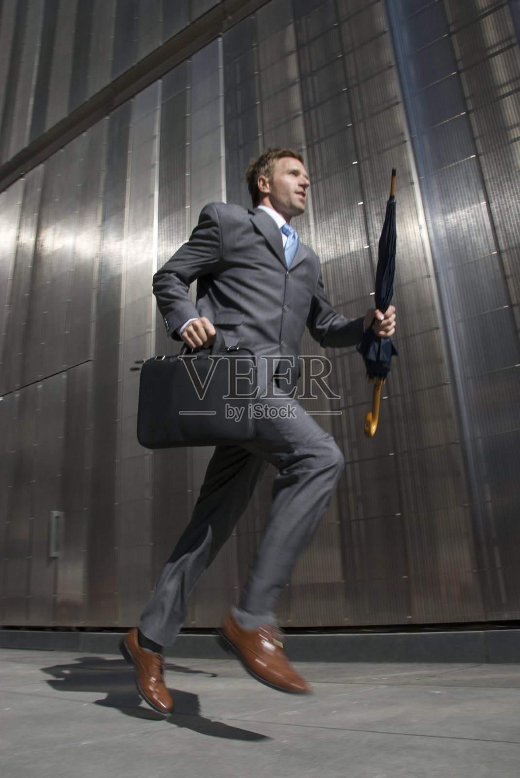 商人在城市的人行道上跑在闪亮的墙前照片摄影图片