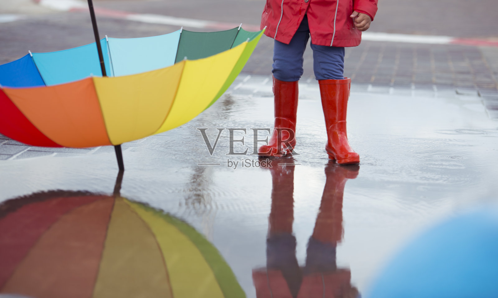 下雨天穿着红靴子打着彩色伞的孩子。照片摄影图片