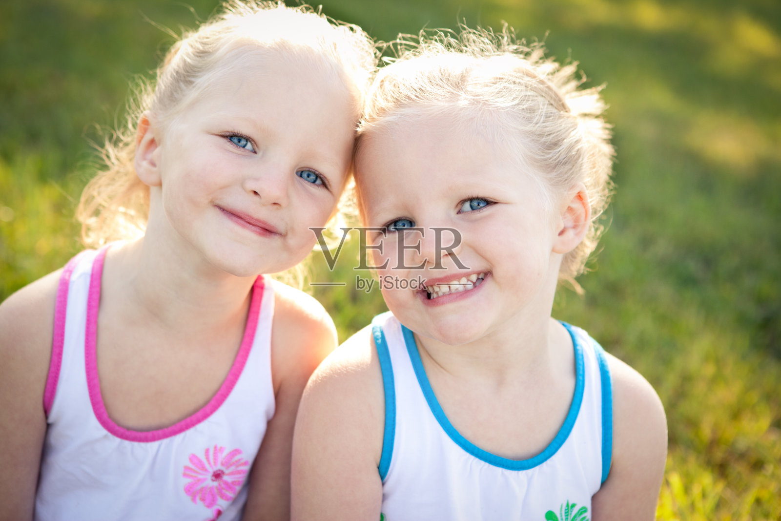 快乐的小双胞胎女孩一起坐在外面的特写照片摄影图片