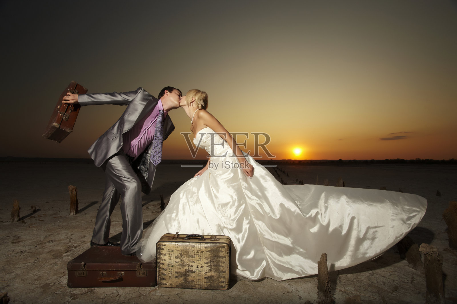 日落沙漠里的新婚夫妇。照片摄影图片